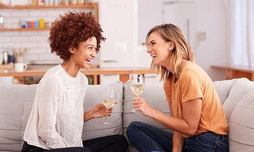 Two women sitting on couch drinking wine and laughing